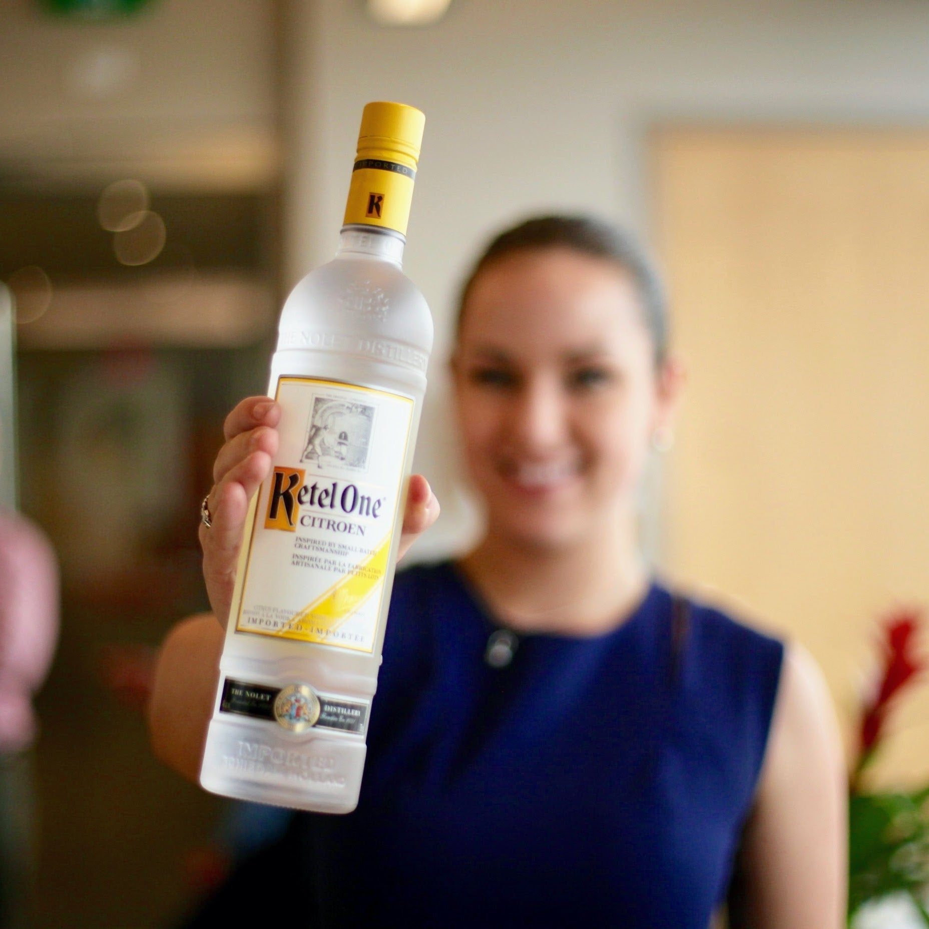 Person holding a bottle of Ketel One vodka in an indoor setting
