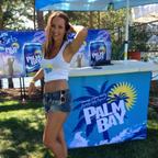 Woman posing in front of a Palm Bay branded booth at an outdoor event.