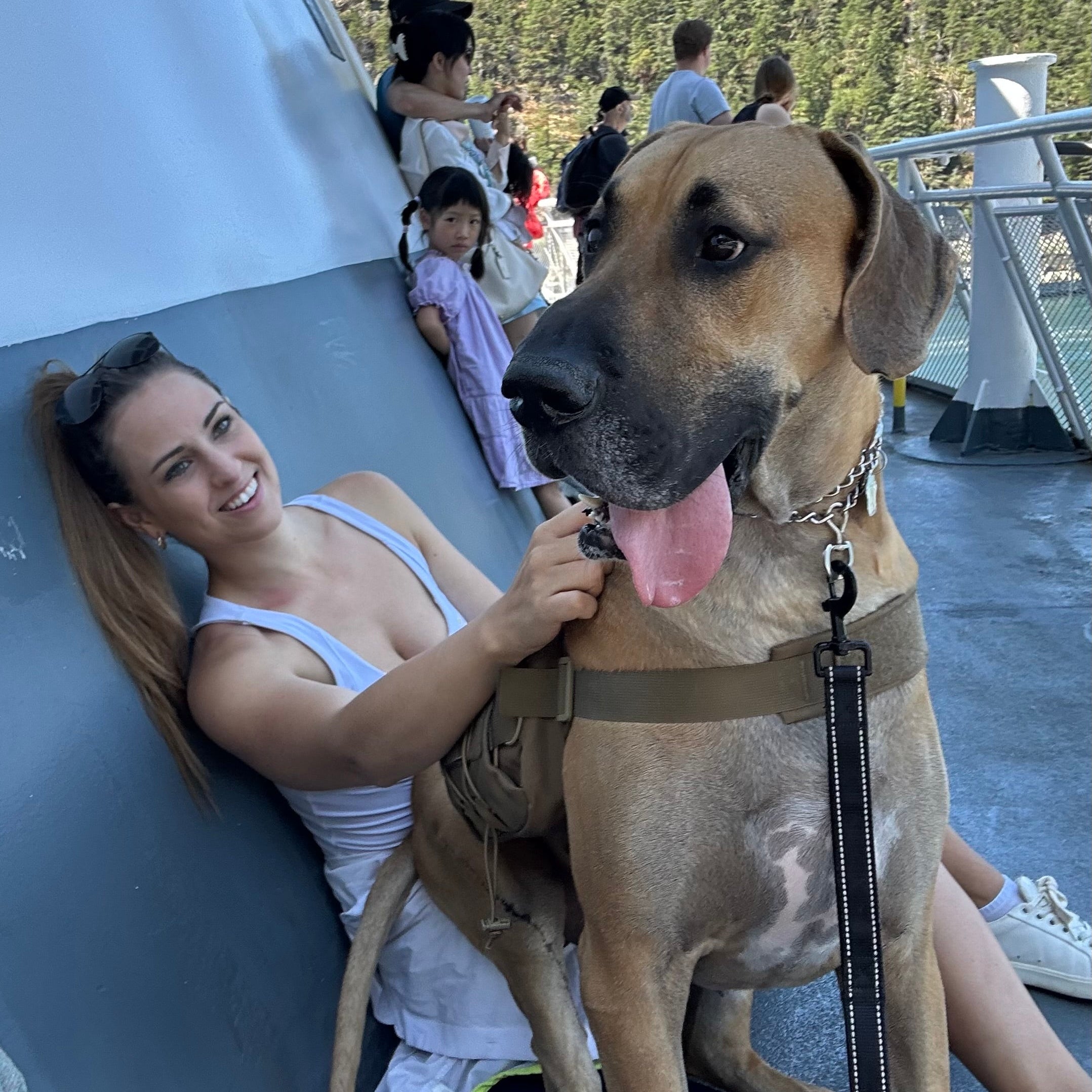 Woman with a large brown dog on a boat deck with people in the background