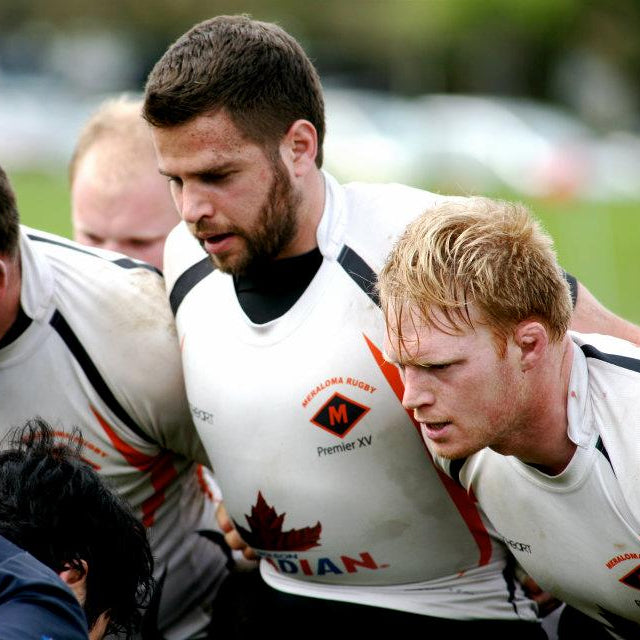 Group of rugby players in white jerseys with a logo on a grass field