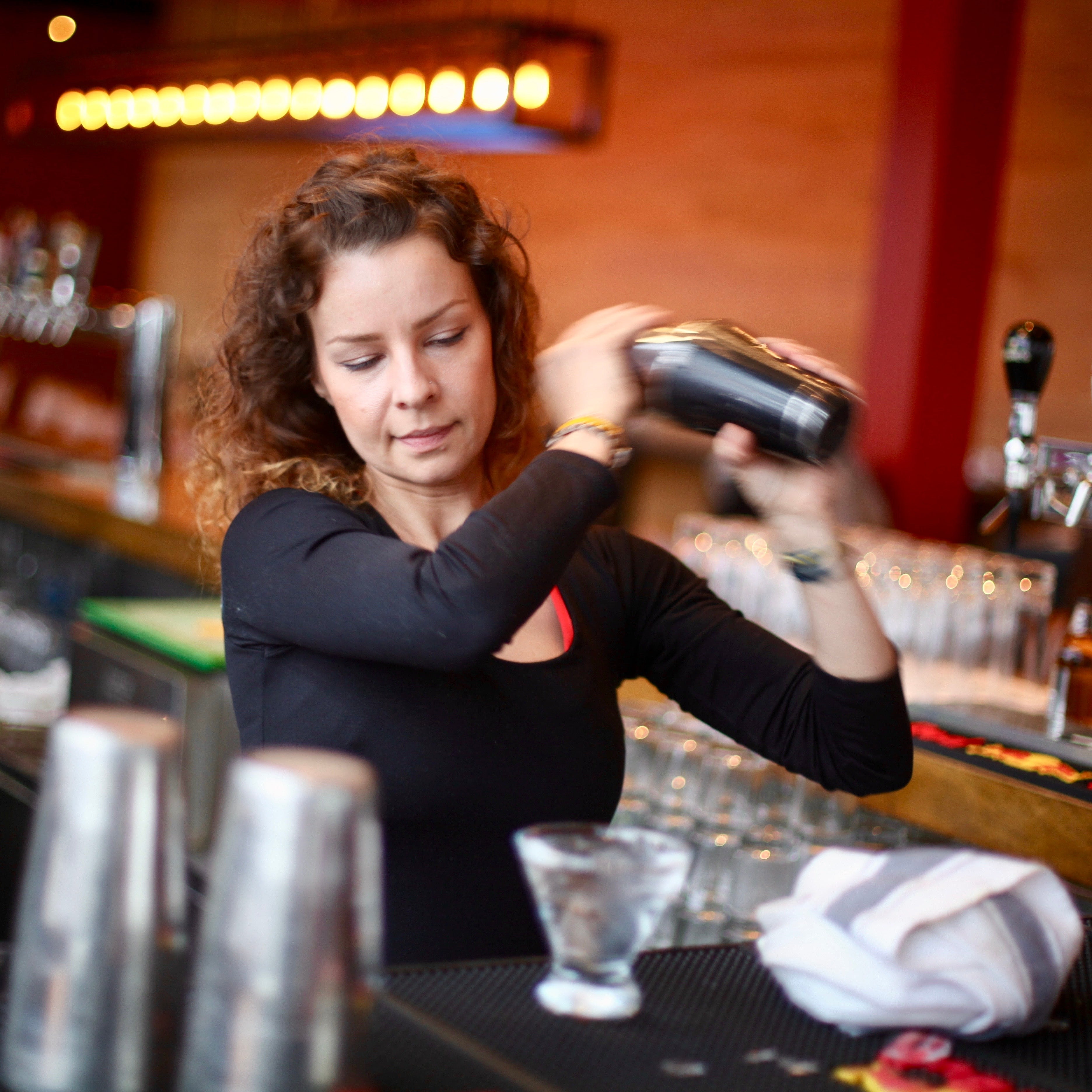 Barista preparing a drink behind the bar with various bottles and glasses in the background.