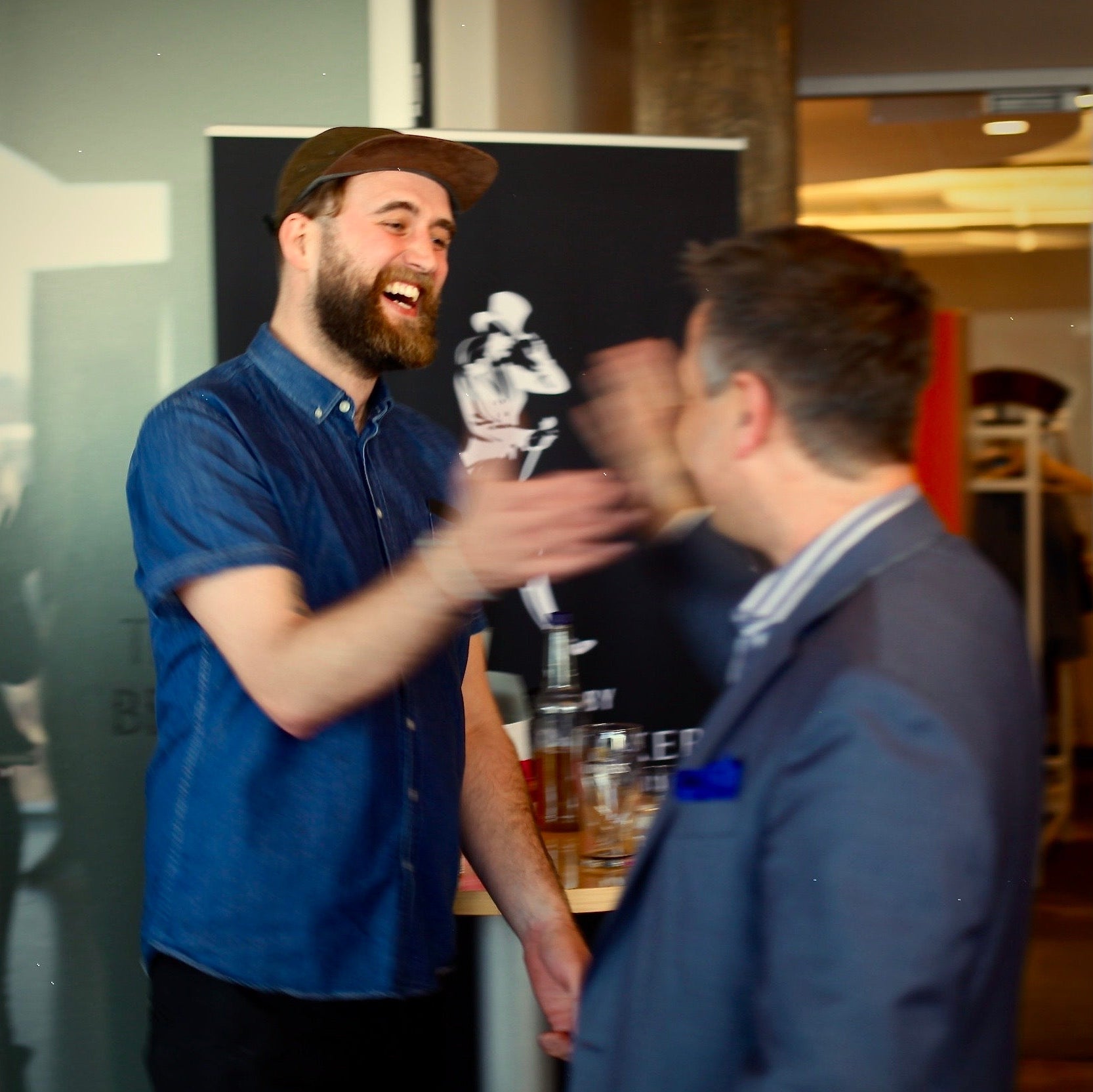 Two men shaking hands in a social setting with drinks and decor in the background.
